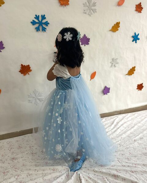 Mi hija de espaldas, con su vestido de princesa celeste, en su cuarto decorado con hojas y copos de nieve de foami que hice para ella.