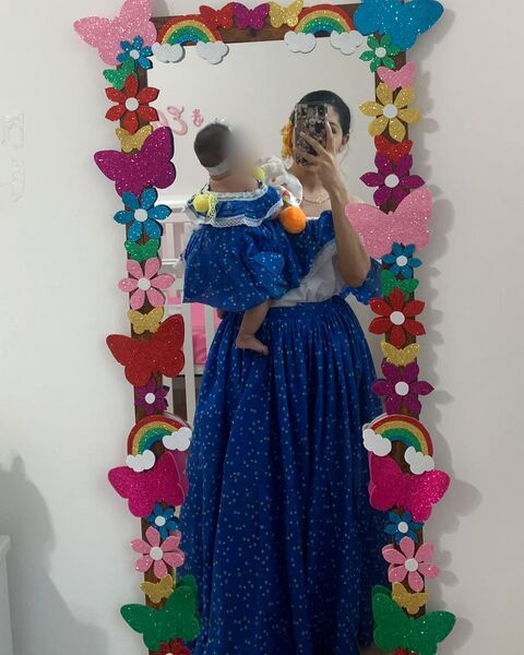 Yo con mi hija en brazos frente al espejo de su cuarto, que decoré con mariposas, flores y arcoíris de foami.