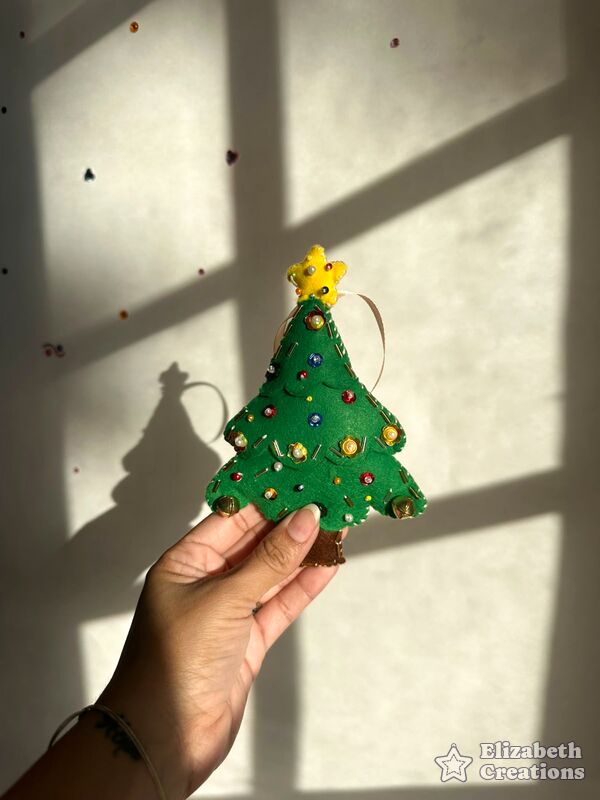 Mano sosteniendo un arbolito de Navidad verde con estrella amarilla en la punta, lentejuelas y perlitas de colores.