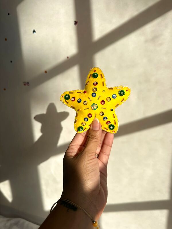 Mano sosteniendo una estrella amarilla, inflada y decorada con lentejuelas verdes y canutillos.