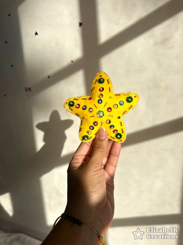 Mano sosteniendo una estrella amarilla, inflada y decorada con lentejuelas verdes y canutillos.