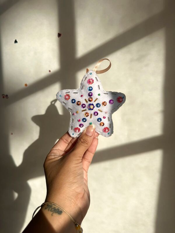 Mano sosteniendo una estrella blanca con una flor de lentejuelas al centro y canutillos de colores.