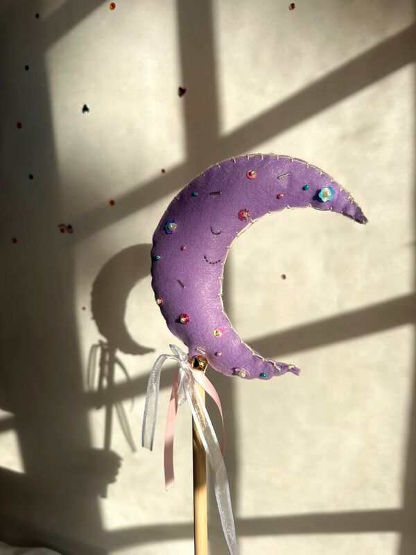 Varita mágica con una luna lila llena de perlitas, a la luz de la ventana.