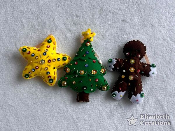 El set Navidad clásica en fila sobre una cobija blanca: una estrella amarilla, un arbolito verde y una galleta de jengibre.