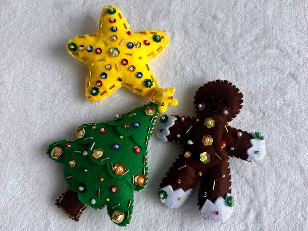 El set Navidad clásica de cerca sobre una cobija blanca: una estrella amarilla, un arbolito verde con su estrellita en la punta y una galleta de jengibre, todos con lentejuelas y perlitas.
