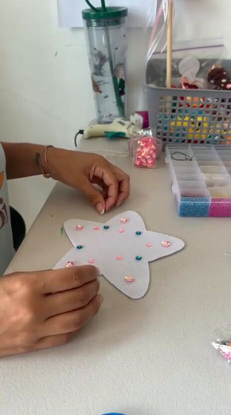 Las manos de Erika en su mesa de trabajo, cosiendo lentejuelas de colores sobre una estrella todavía plana, entre cajitas de perlitas y cintas.